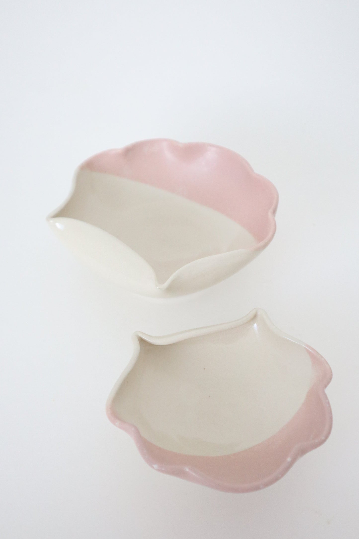Two pink and white ceramic sea shells on a light gray background