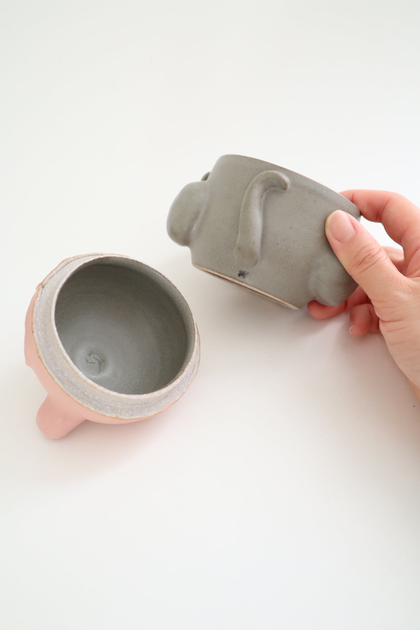 Hand holding a gray ceramic cat jar against a white background