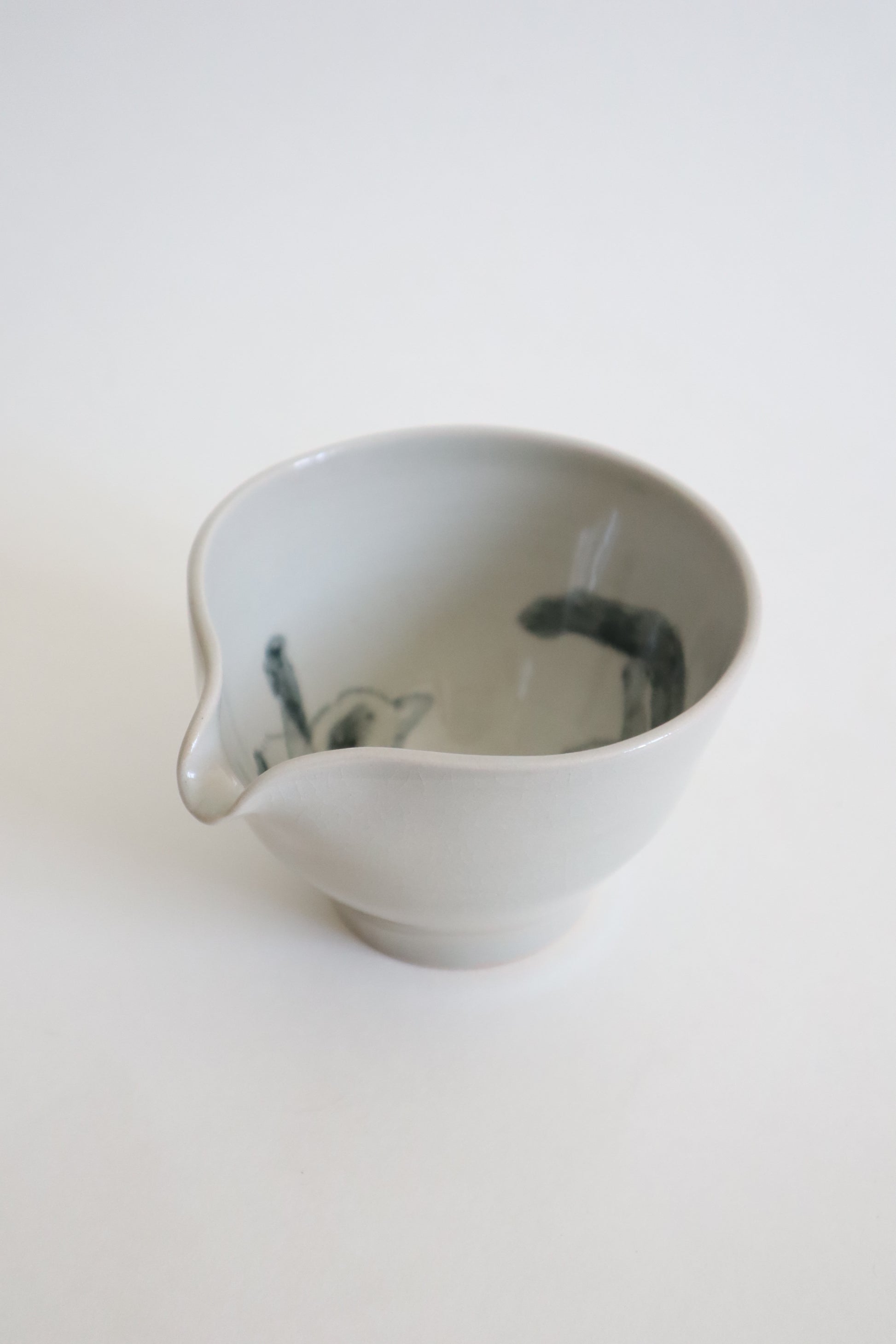A small white ceramic pitcher with a dark green hand-painted fish design inside, shown on a plain white background.