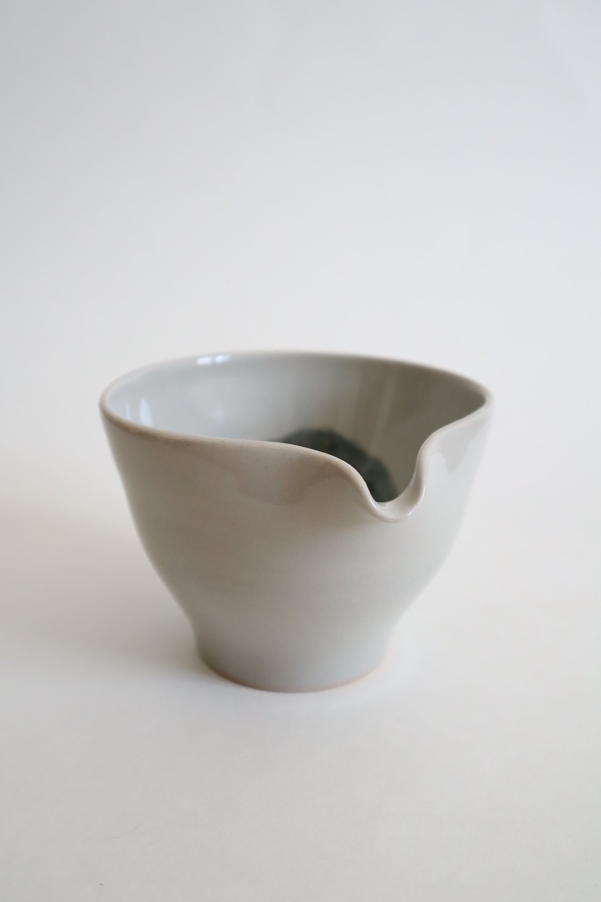 A minimalist ceramic pitcher with a small pouring spout, featuring a matte light gray exterior and a glossy dark gray interior, set against a clean off-white background.